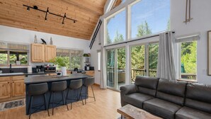 A modern kitchen with a central island, bar stools, and a large window overlooking a deck. - Raven Haven Lodge 2 Bedroom Home by RedAwning (Leavenworth)