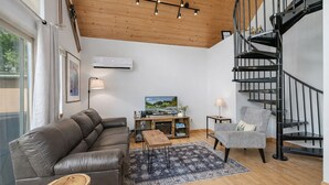 A modern living room with a leather sofa, a patterned armchair, a wooden coffee table, a TV, and a black spiral staircase. - Raven Haven Lodge 2 Bedroom Home by RedAwning (Leavenworth)