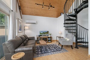 Een moderne woonkamer met een leren bank, een fauteuil met patroon, een houten salontafel, een televisie en een zwart spiraaltrap.