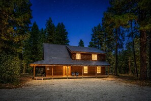 A two-story log cabin with a porch, surrounded by a forest.