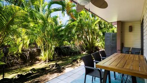 Een terras met een houten tafel en stoelen, omgeven door weelderige begroeiing en een betegelde vloer.