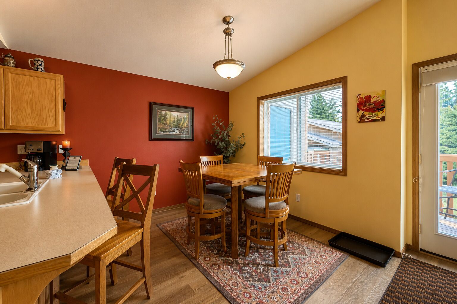A dining area with a wooden table and chairs, a kitchen with a sink and cabinets, a framed picture on the wall, and a window with blinds.