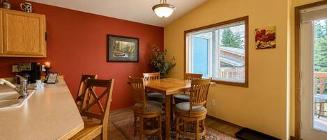 A dining area with a wooden table and chairs, a kitchen with a sink and cabinets, a framed picture on the wall, and a window with blinds.