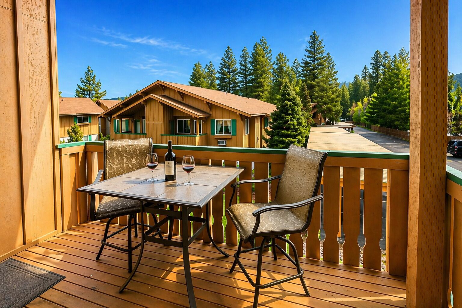 Une terrasse en bois avec une table et des chaises, une bouteille de vin et une vue sur des chalets dans une forêt.