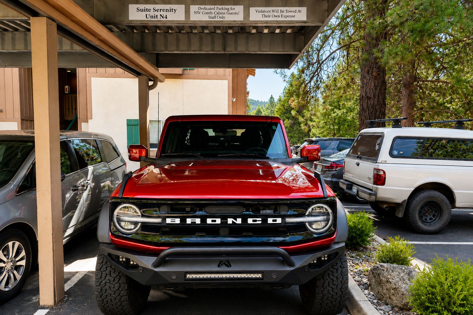 Um Bronco vermelho estacionado em uma área de estacionamento coberta com uma placa indicando 'Suite Serenity Unit N4' e 'Estacionamento Dedicado para Hóspedes dos NW Comfy Cabins'.