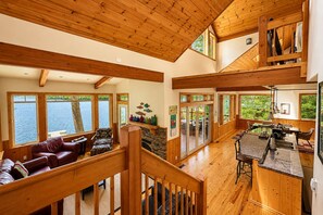 Un interior espacioso con una escalera de madera, un comedor y grandes ventanales con vistas al agua.
