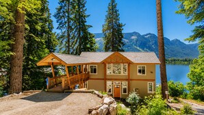 Un chalet doté d’une terrasse en bois, d’un porche et offrant une vue sur un lac et des montagnes.