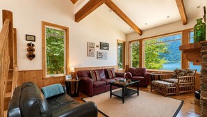 L’intérieur d’une cabane est agrémenté d’un escalier en bois, d’un canapé en cuir, d’un divan rouge, d’une table basse et de grandes fenêtres qui offrent une vue sur un lac.