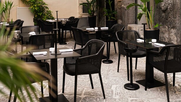 An outdoor café with stone flooring, black wicker furniture, and potted plants. - Relais Metis (Naples)