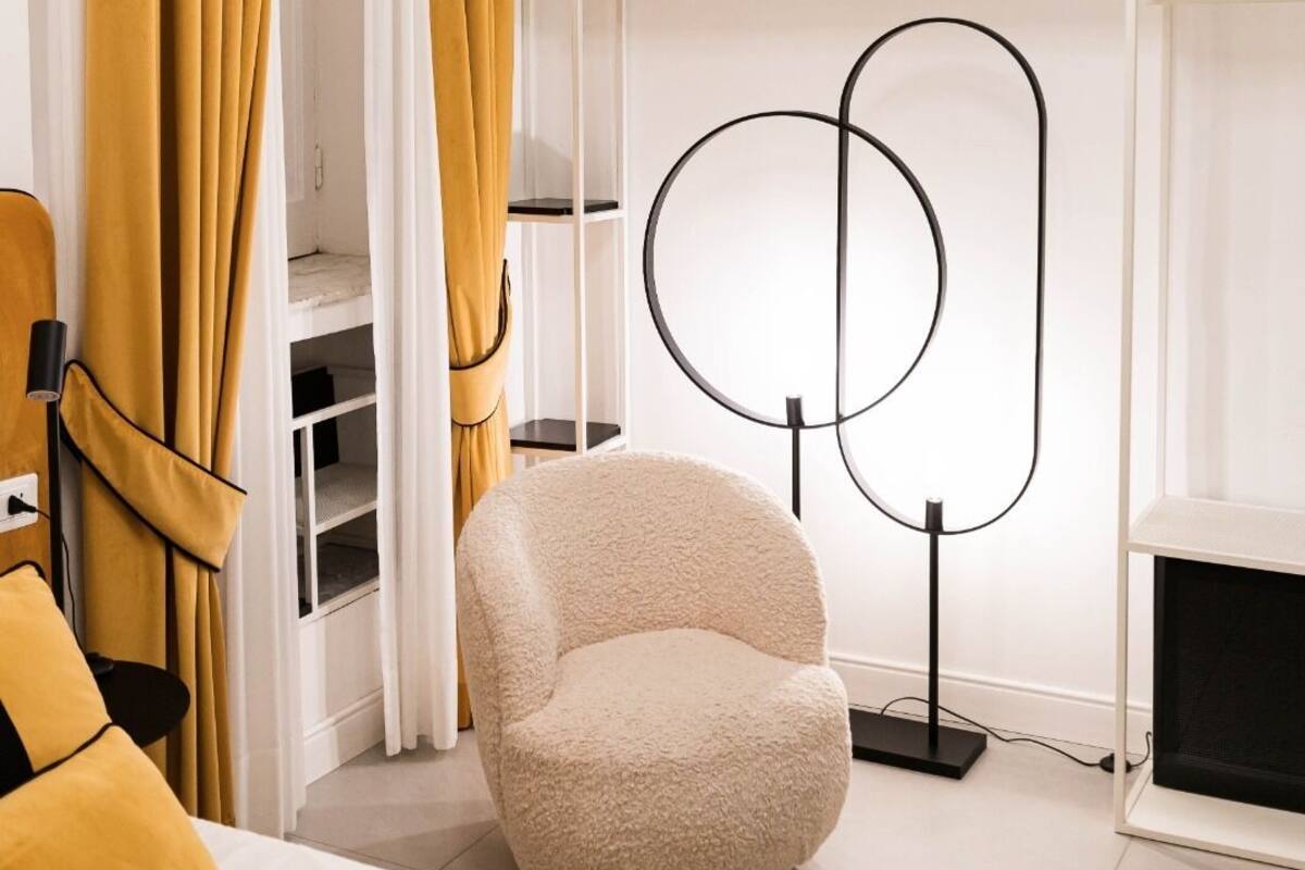 Une chambre à coucher moderne avec un lit, un fauteuil moelleux, une lampe sur pied et une armoire.