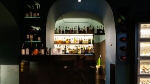 A bar area with a dark interior, a counter with bottles, and two green chairs. - Relais Metis (Naples)