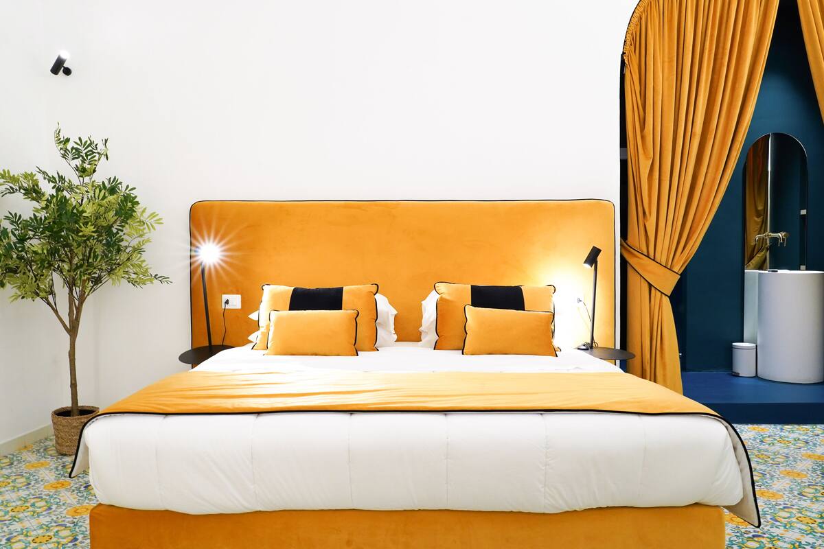 Un lit avec une tête de lit blanche et orange, une plante en pot et un miroir dans une salle de bain.