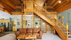 A spacious living room with a leather sofa, a wooden coffee table, and a wooden staircase with a railing. - Riffle River Lodge 3 Bedroom Home by NW Comfy Cabins by RedAwning (Leavenworth)
