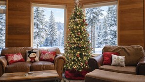 A cozy living room with a Christmas tree, leather sofas, and large windows overlooking a snowy forest. - Riffle River Lodge 3 Bedroom Home by NW Comfy Cabins by RedAwning (Leavenworth)