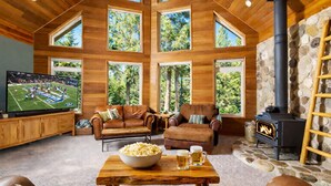 A cozy living room with a stone fireplace, leather furniture, and a television displaying a football game. - Riffle River Lodge 3 Bedroom Home by NW Comfy Cabins by RedAwning (Leavenworth)
