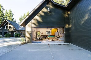 Une maison dont la porte du garage est ouverte, dévoilant un salon avec une table de billard, un canapé et un coin cuisine.