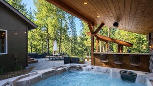 A hot tub area with a wooden pergola overhead, surrounded by outdoor seating and a view of a forested area. - Riffle River Lodge 3 Bedroom Home by NW Comfy Cabins by RedAwning (Leavenworth)