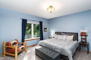 Une chambre à coucher comprenant un lit, un banc, une chaise, une table de chevet, une lampe et une fenêtre avec des rideaux.
