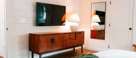 A bedroom with a wooden dresser, a flat-screen TV mounted above it, and a mirror on the wall.