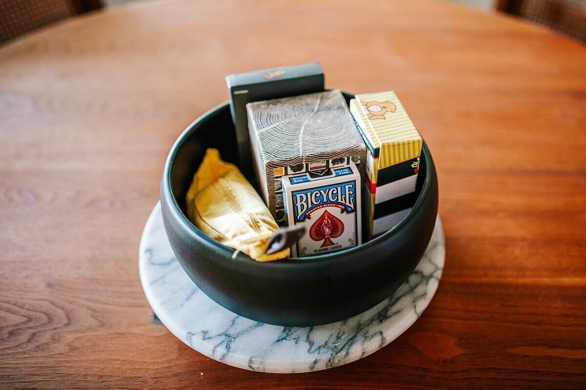 A bowl containing a pack of Bicycle brand cigarettes, a lighter, and a pack of cigarettes on a marble coaster.