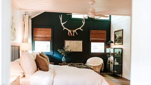 Ein Schlafzimmer mit einem Bett, einem Sessel, einem Heizkörper, einem Deckenventilator und einem an der Wand befestigten Hirschgeweih.