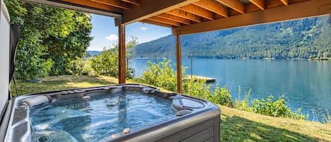 Ein Whirlpool unter einer Hollaube mit Blick auf einen See und Wald.