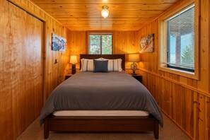 A wooden-paneled bedroom with a bed, two bedside lamps, and a window with blinds. - All About The Lake 4 Bedroom Home by NW Comfy Cabins by RedAwning (Leavenworth)