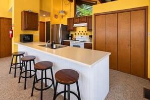Une cuisine dotée d’un îlot central, de tabourets de bar, de meubles en bois, d’appareils électroménagers en acier inoxydable et d’un extincteur.