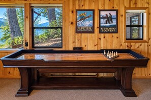 Une table de billard en bois, placée devant de grandes fenêtres offrant une vue sur un paysage montagneux.