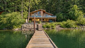 A wooden cabin with a balcony overlooking a lake, surrounded by dense forest.