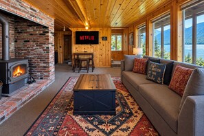 A cozy living room with a fireplace, a sofa, a coffee table, and a television displaying 'NETFLIX'. - All About The Lake 4 Bedroom Home by NW Comfy Cabins by RedAwning (Leavenworth)