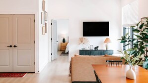 A modern living room with a wooden dining table, a sofa, and a TV mounted on the wall.
