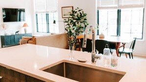 A kitchen with a stainless steel sink, a vase with green leaves, and two bottles of hand soap.