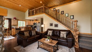 A spacious living area with a brown leather sofa set, a wooden coffee table, and a staircase with a wooden railing.