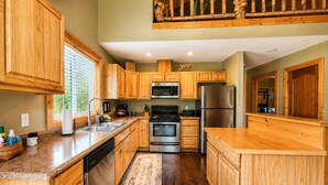 A kitchen with wooden cabinets, stainless steel appliances, and a window with blinds.