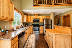 A kitchen with wooden cabinets, stainless steel appliances, and a window with blinds.
