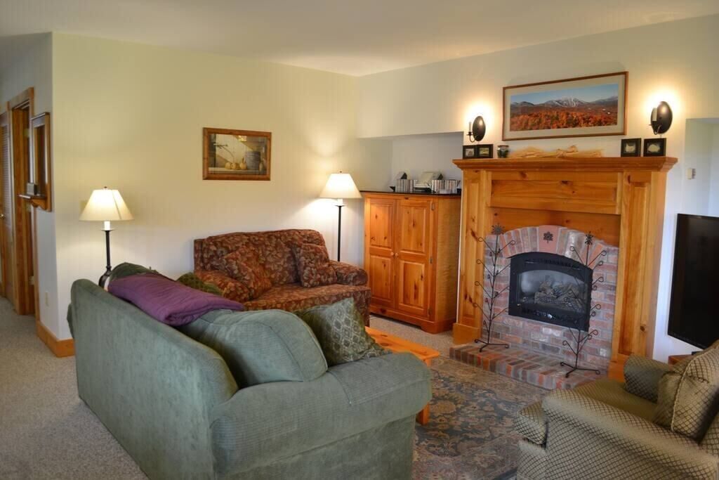 Una sala de estar con chimenea, un sofá, un sillón estampado y un aparador.