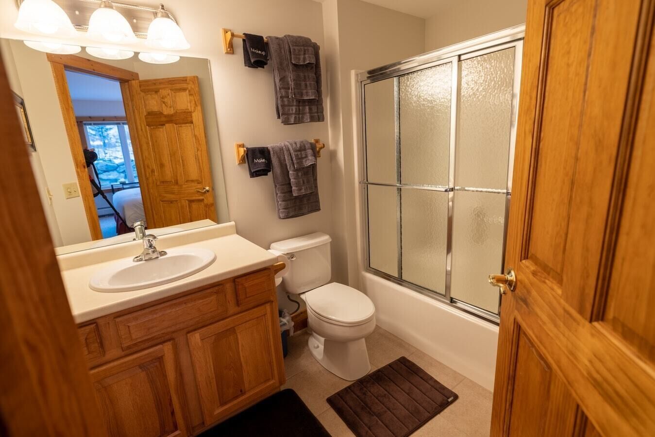 Un baño con tocador de madera, lavamanos blanco, inodoro y cabina de ducha de cristal.