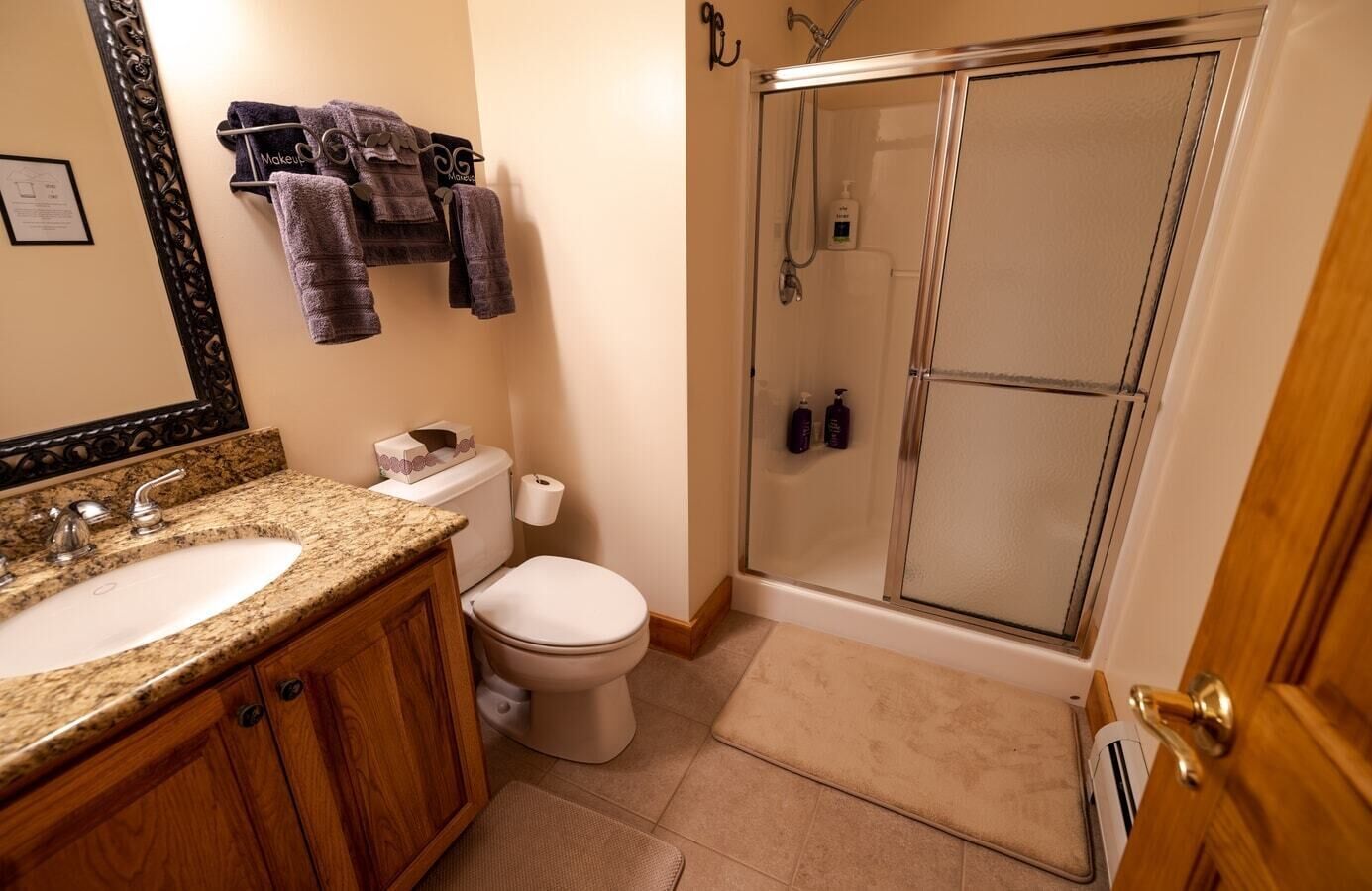 Een badkamer met twee wastafels, een toilet, een douche met glazen deuren en handdoeken aan een rek.