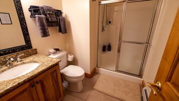 Een badkamer met twee wastafels, een toilet, een douche met glazen deuren en handdoeken aan een rek.
