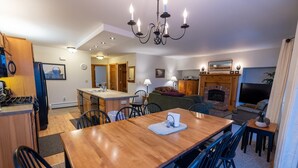 A modern kitchen with a central island, a dining area with a wooden table and chairs, a living room with a fireplace, and a TV.