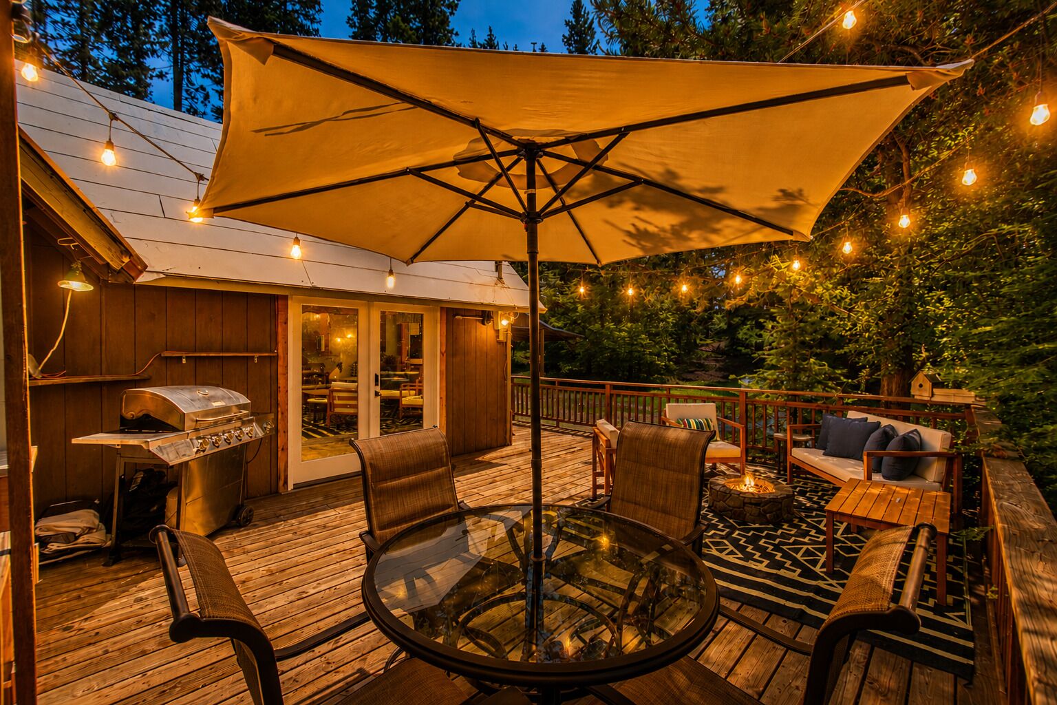 Una terraza con mesa de vidrio, sillas y una parrilla.