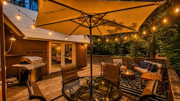 Una terraza con mesa de vidrio, sillas y una parrilla.