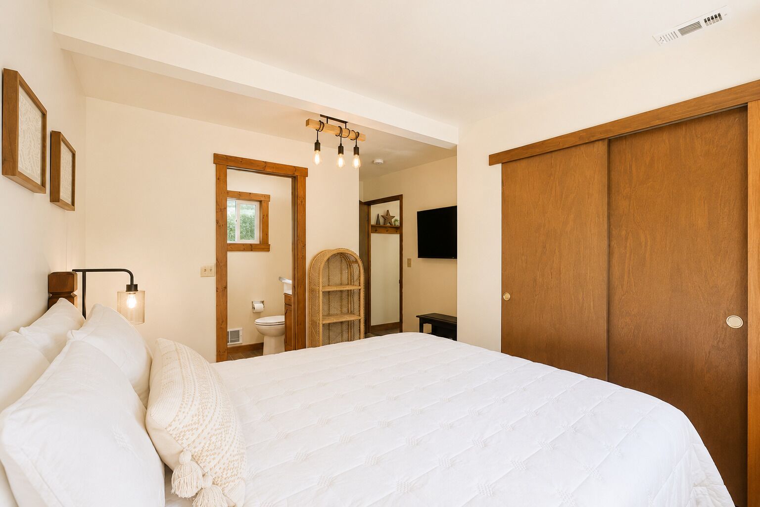 Ein Schlafzimmer mit einem großen Bett, einem Holzschrank, einem Nachttisch, einem an der Wand montierten Fernseher und einem Fenster mit Blick ins Freie.