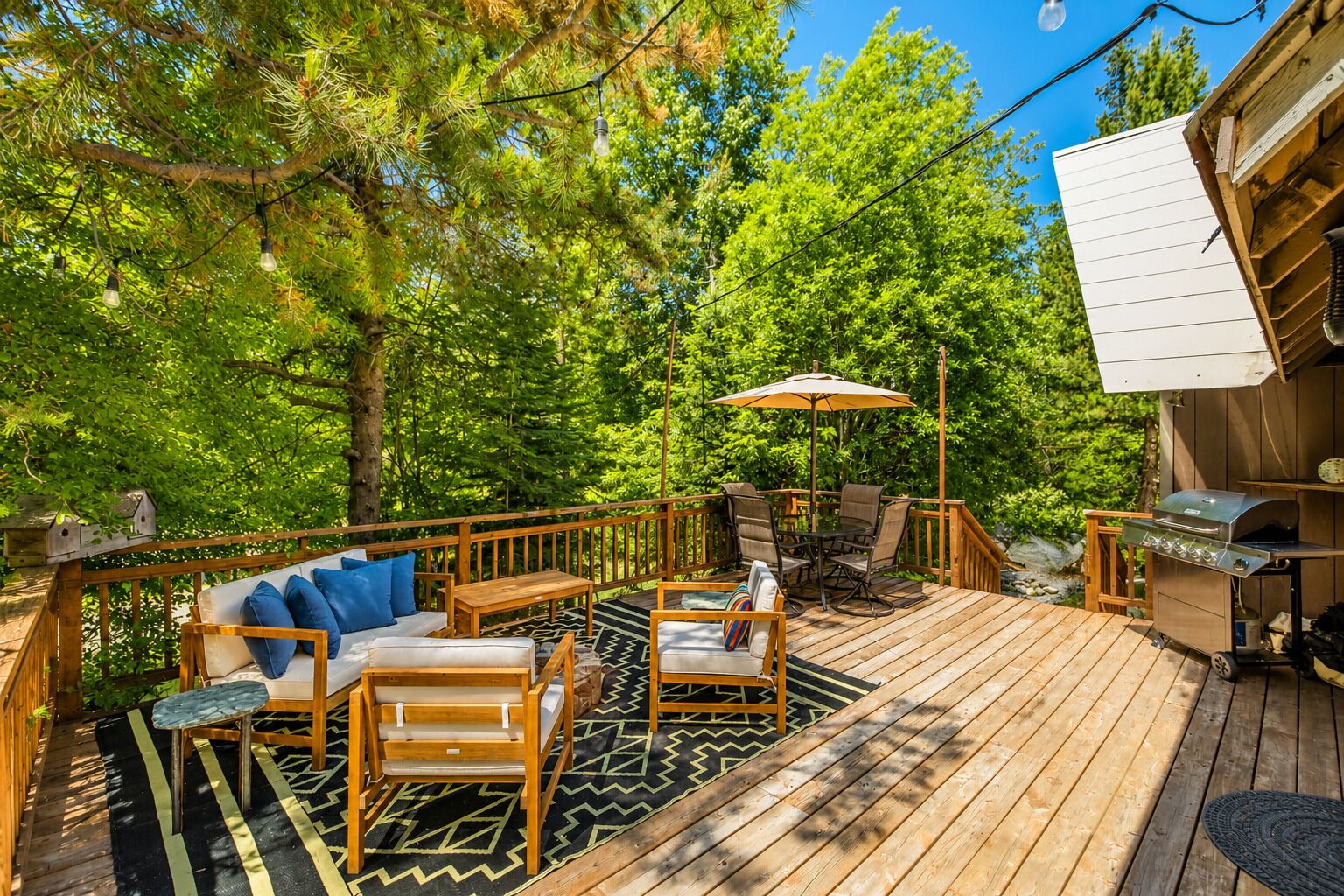 A wooden deck with outdoor furniture, a grill, and a view of the surrounding forest.