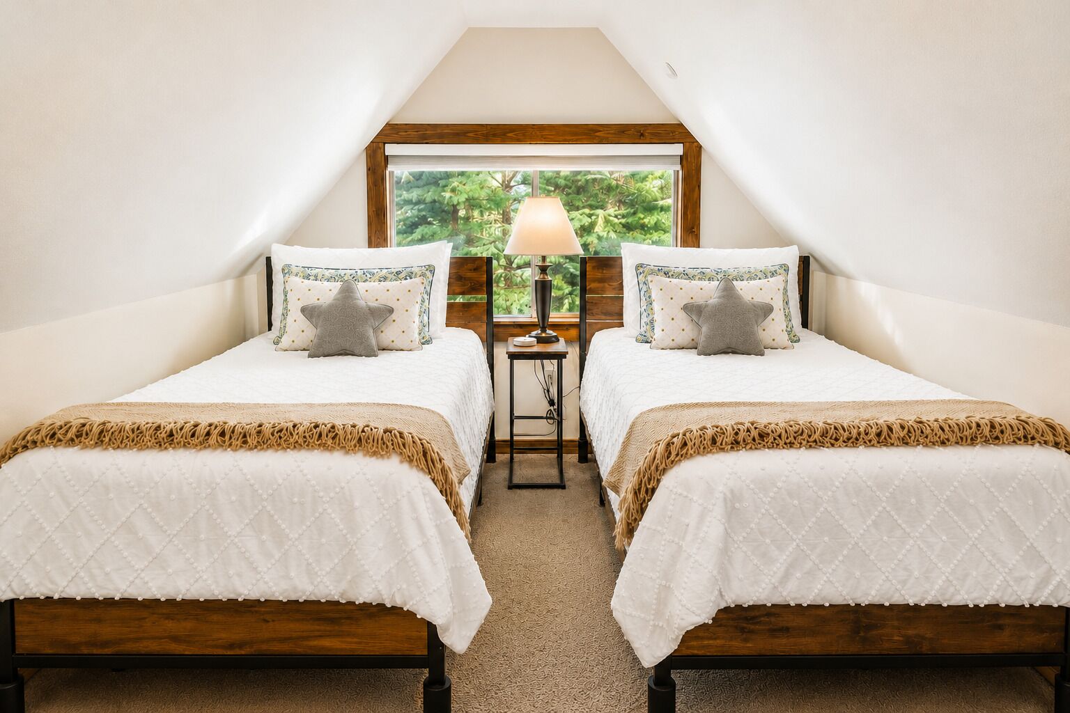 A bedroom with two beds, a nightstand, a lamp, and a window with a view of greenery.