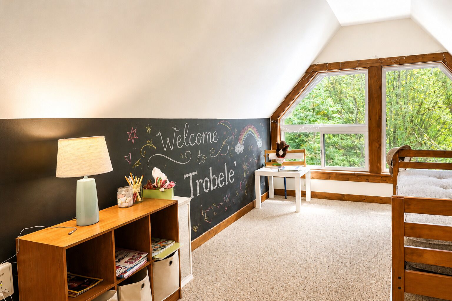 Une chambre d’enfant avec un mur recouvert d’un tableau noir, un bureau, un lit et une fenêtre donnant sur un paysage verdoyant.