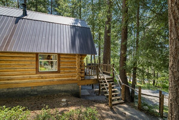 A log cabin with a metal roof, a wooden staircase, and a window.