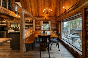 A log cabin interior with a dining area, kitchen, and large windows overlooking a deck. - Guten Cabin 3 Bedroom Home by NW Comfy Cabins by RedAwning (Leavenworth)