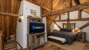 Ein rustikales Schlafzimmer mit Holzbalkendecke, einem Bett, einem Wandfernseher und einem Schild mit der Aufschrift 'MOUNTAIN Time'.
